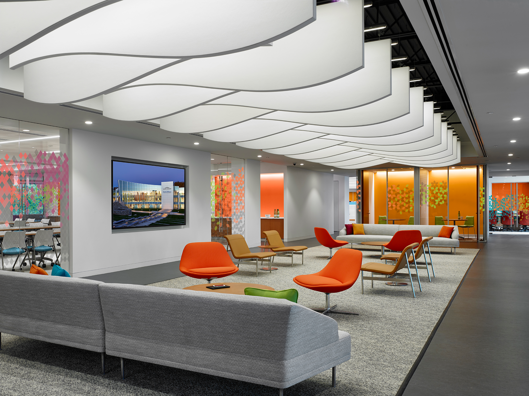 Beautiful white ceiling panels that look like waves drop down over a seating area with two grey couches and several chairs with tables.