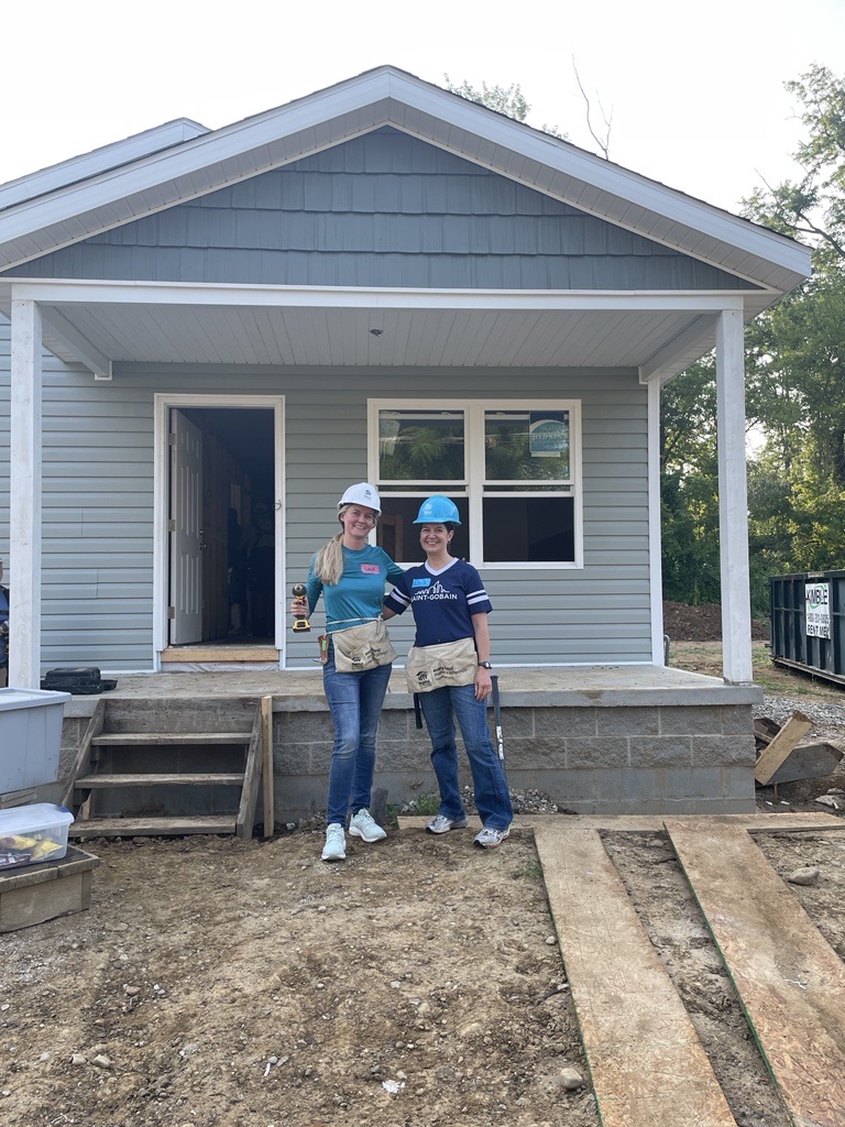 Two women wearing hard hats stand in front of a home under construction