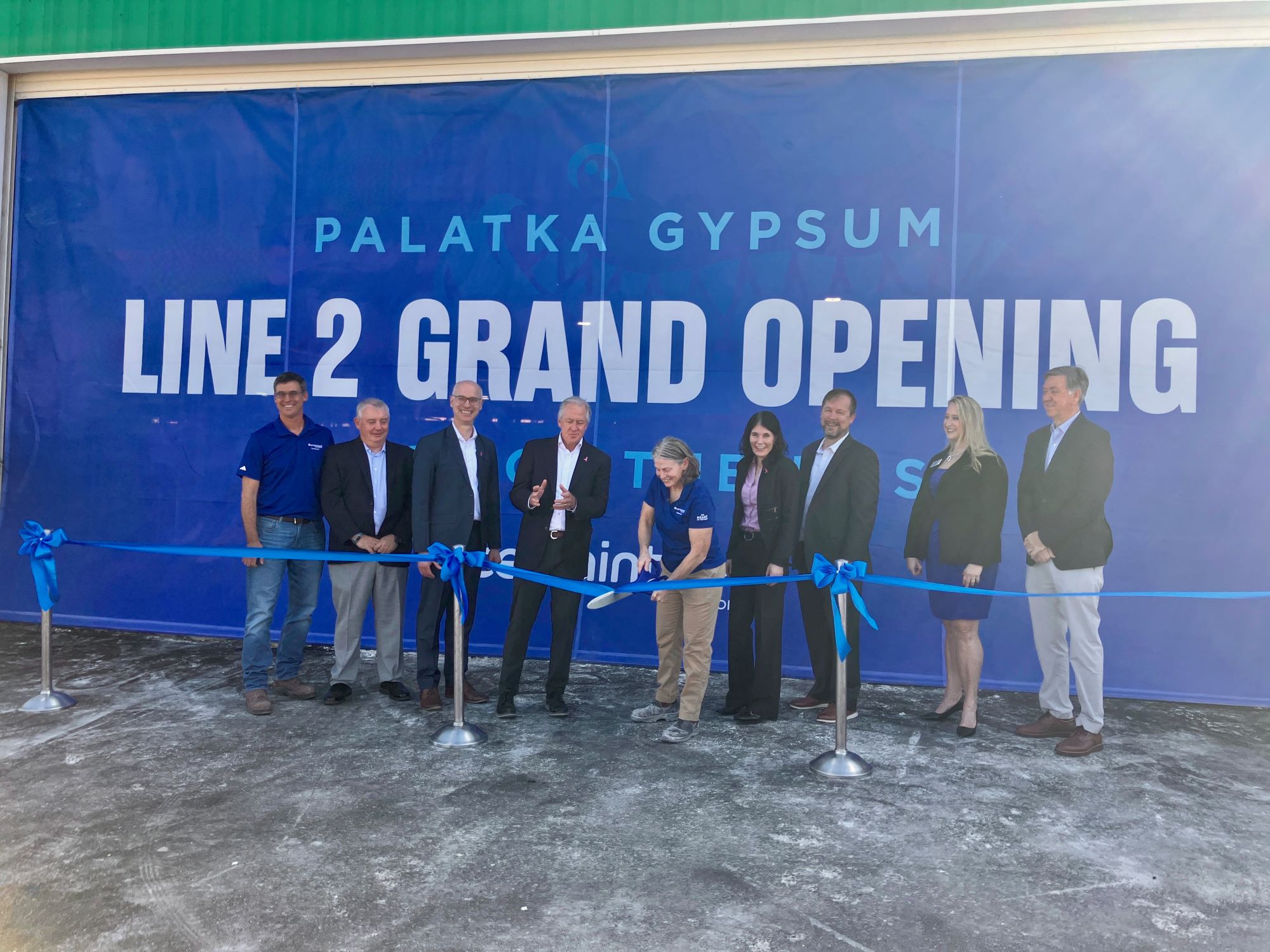 /9%20people%20stand%20in%20front%20of%20a%20sign%20that%20reads%20%22Palatka%20Gypsum%20Line%202%20Grand%20Opening%22%20while%20the%20female%20Plant%20Manager%20in%20the%20center%20cuts%20the%20ribbon