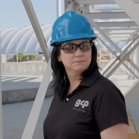 A woman with a blue GCP hard hat stands outside at the factory