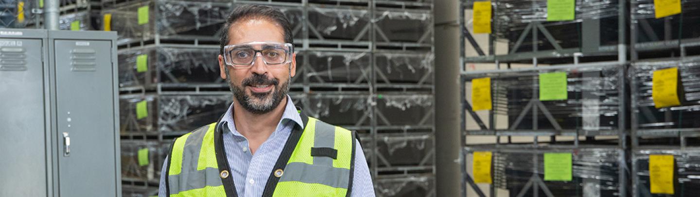 A Man wearing a yellow safety vest and goggles stands in a warehouse setting