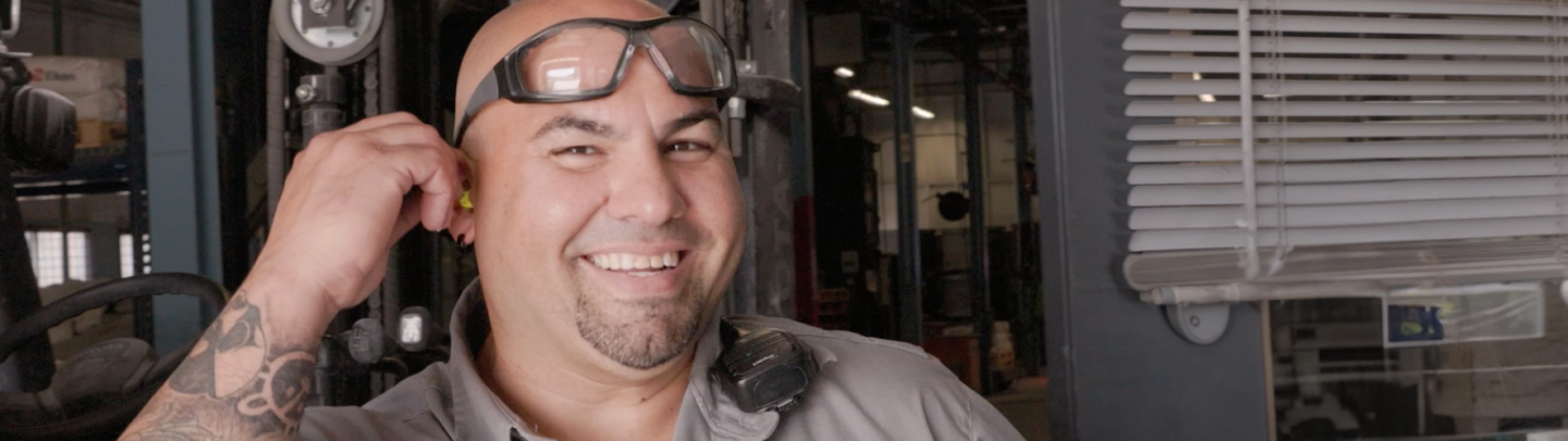 Man with safety goggles on his head is putting in ear protecting and smiling