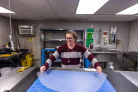 A woman is an a drafting table placing a clear material down.