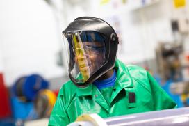 A Black man wearing a facial shield works in the manufacturing plant 