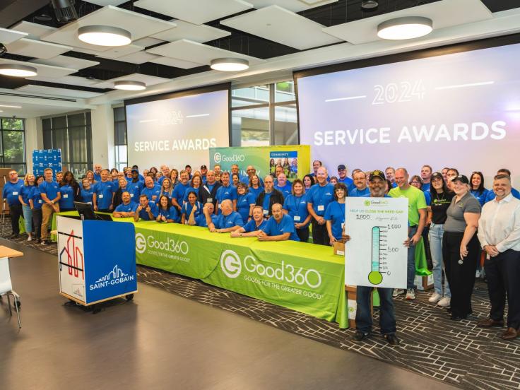 A large group of people watching matching t-shirts stand behind a Good360 table