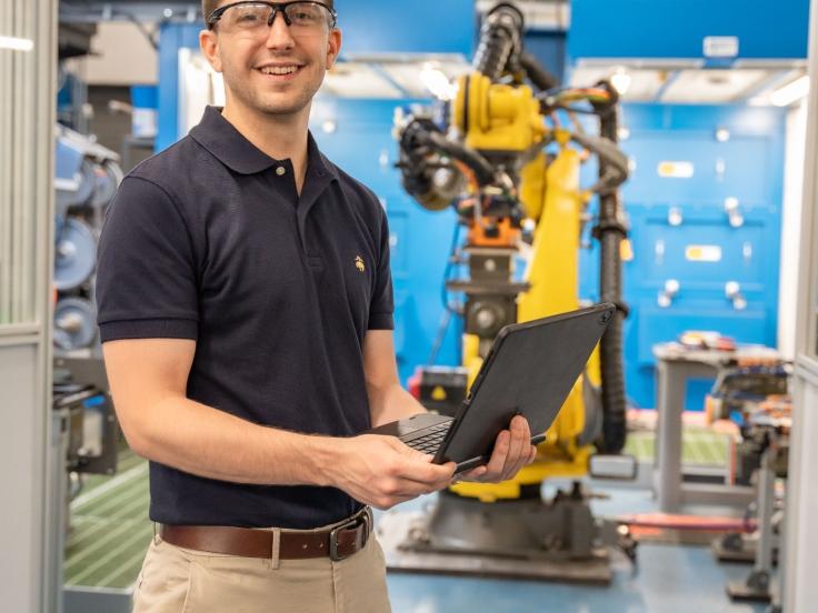 Industrial engineer with a laptop in a modern automated manufacturing and robotics facility.