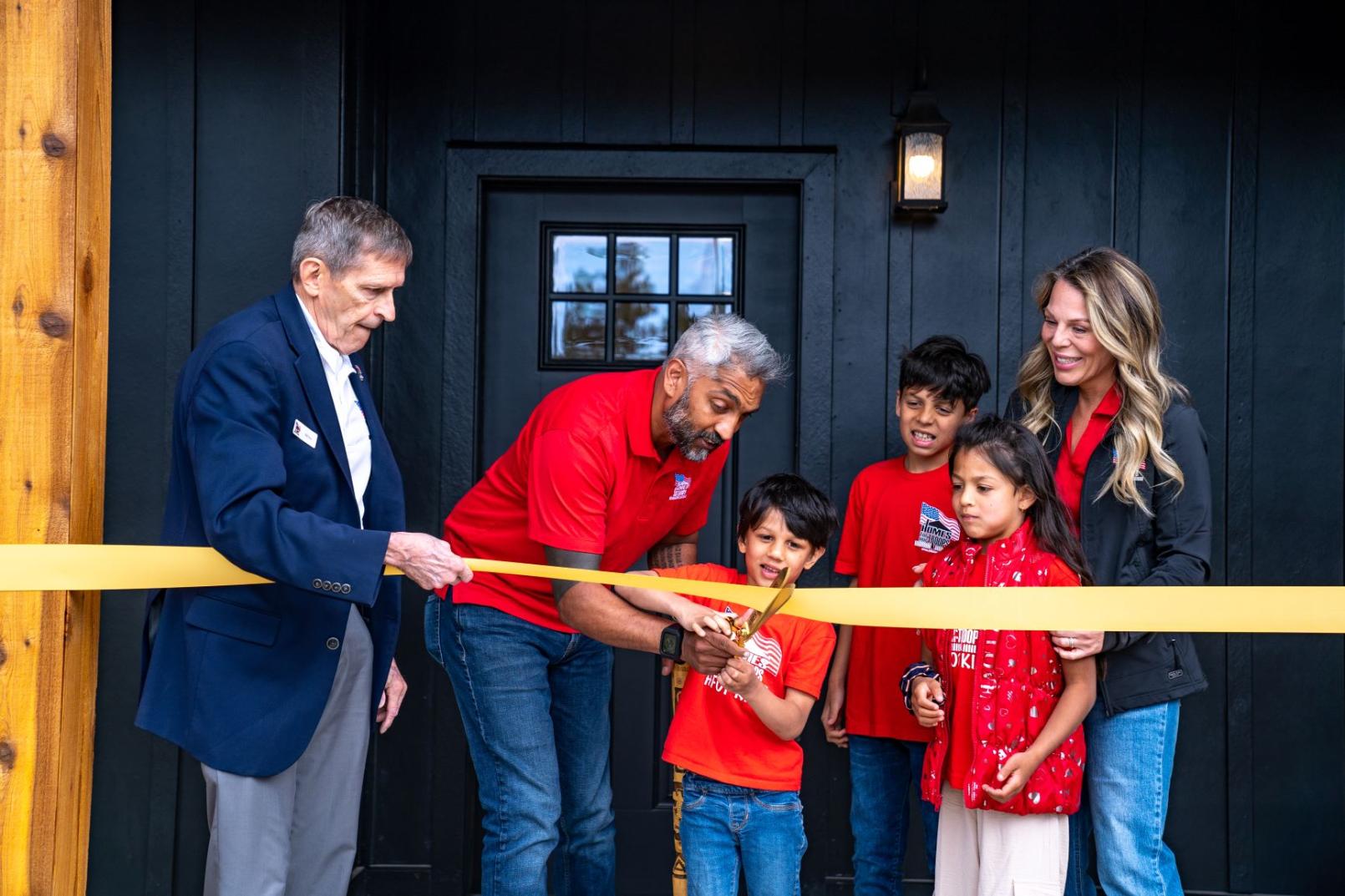 A family wearing red is cutting the yellow ribbon in front of their new home