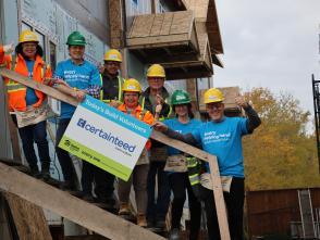 Seven people wearing hard hats are standing on stairs being build holding a sign that says "Today's Build Volunteers" with CertainTeed's logo