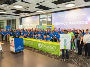 A large group of people watching matching t-shirts stand behind a Good360 table