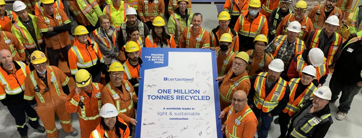 A large group of people in safety vets and hard hats gather around a sign that says One Million Tonnes Recycled