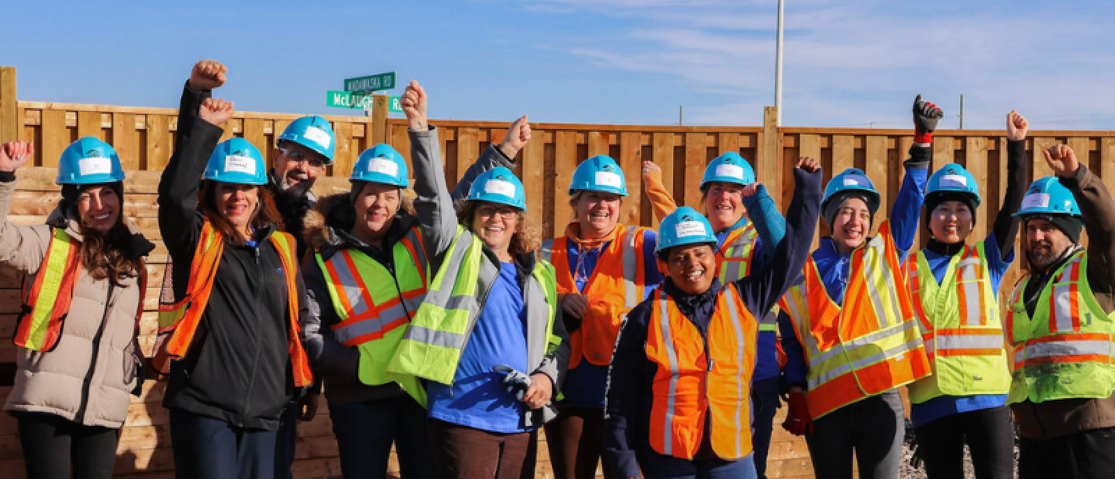 A group of people wearing safety vests and hard hats posting for a photo 