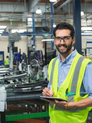Employee wearing a high-visibility safety vest using a tablet while overseeing manufacturing operations in a modern factory.