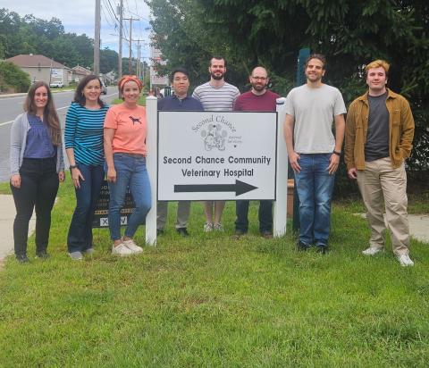 Eight people stand around a sign that says "Second Chance Community Veterinary Hospital"